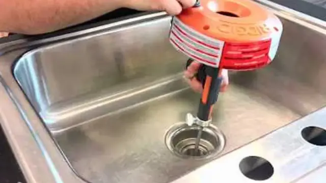 Plumber feeding a drain auger into a kitchen sink drain